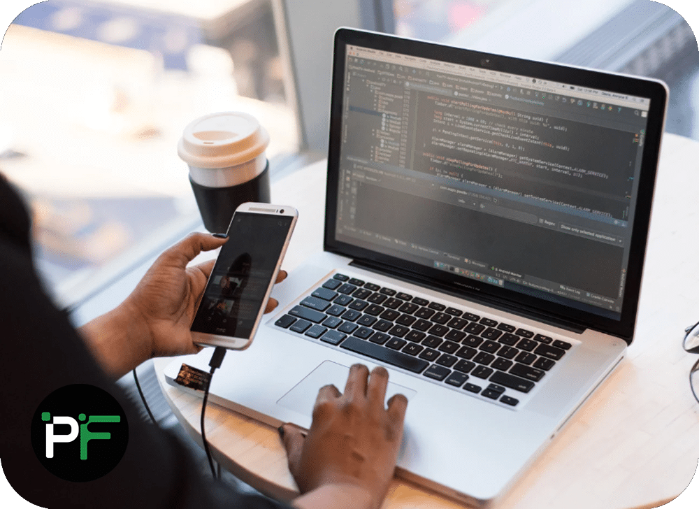 Software developer working on their laptop and using their phone to demonstrate multi device technology stack solutions